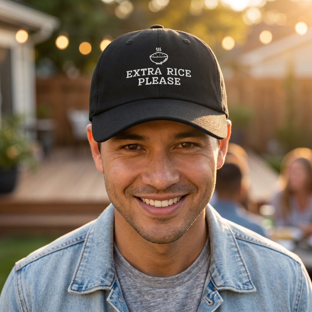 Man wearing a black cap with 'Extra Rice Please' text, smiling outdoors.