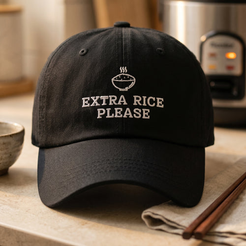 Black cap with 'Extra Rice Please' text on a kitchen counter