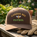 Brown cap with 'Garden Bee Patrol' text and a bee logo on a wooden surface with gloves.