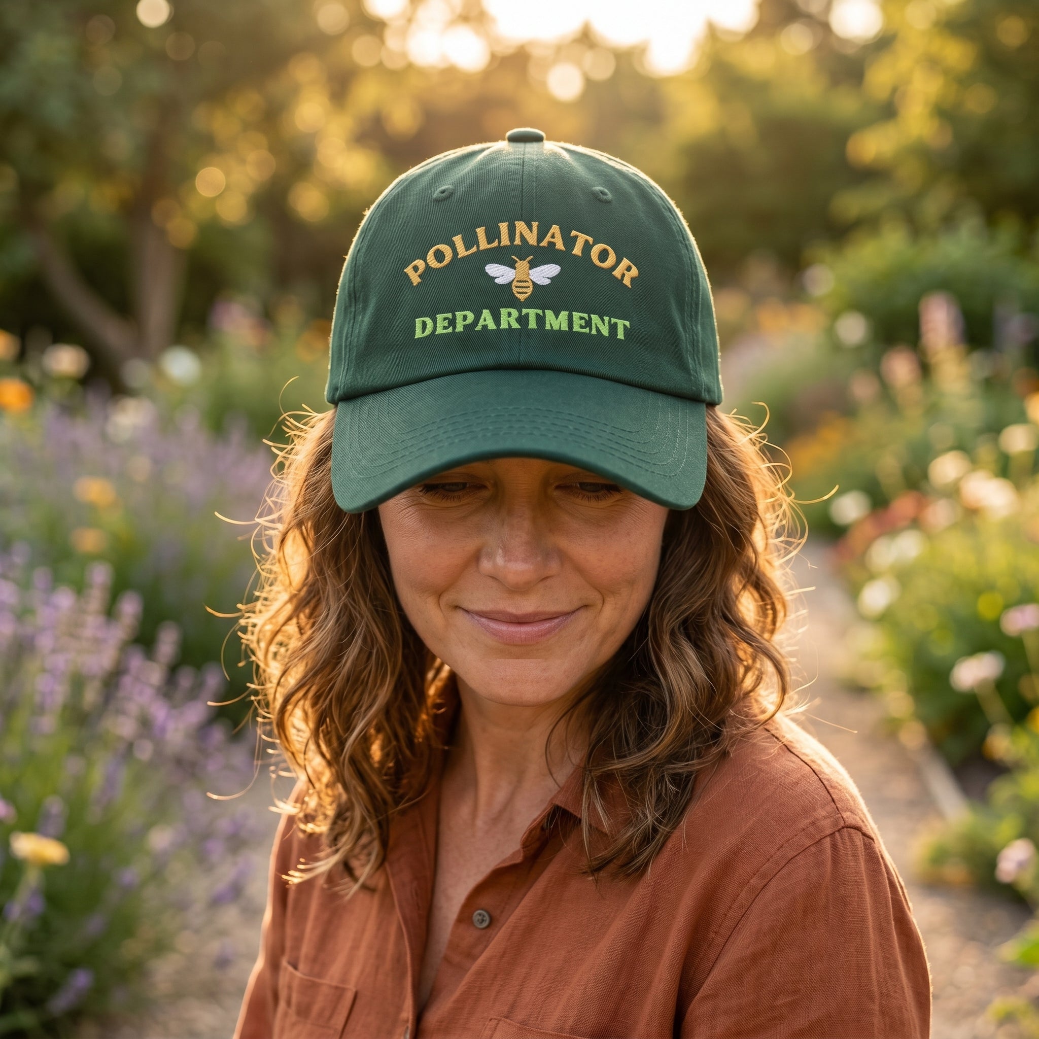 Woman wearing a green 'Pollinator Department' cap in a garden setting